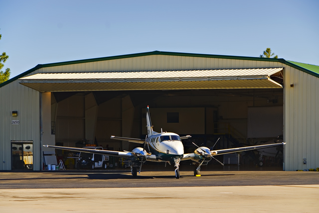 airplane parked in front of steel building with large open bifold door.