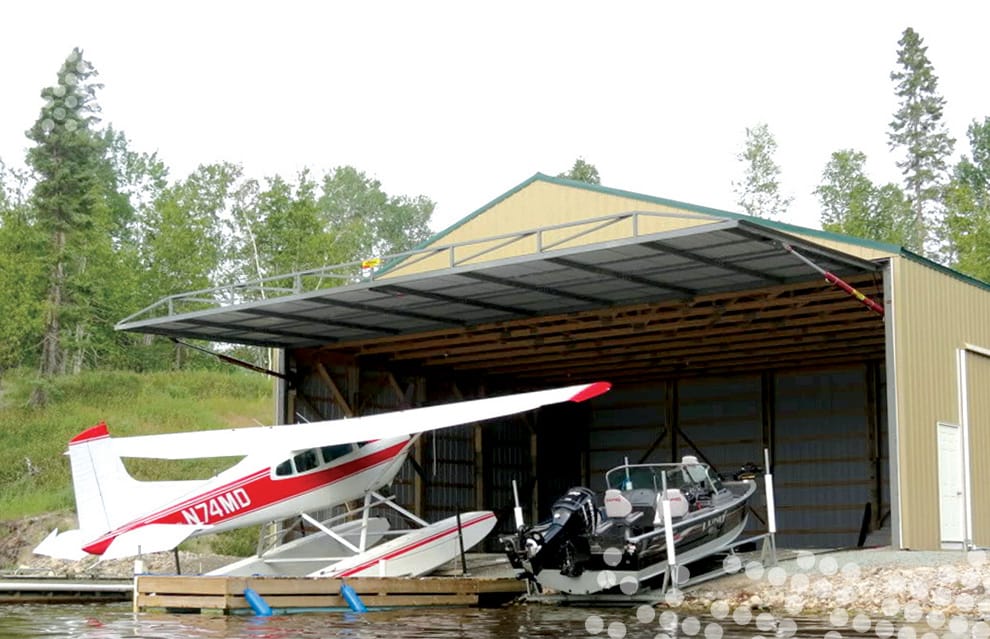 Float plane and boat parked in front of boathouse fitted with Schweiss hydraulic door shown open