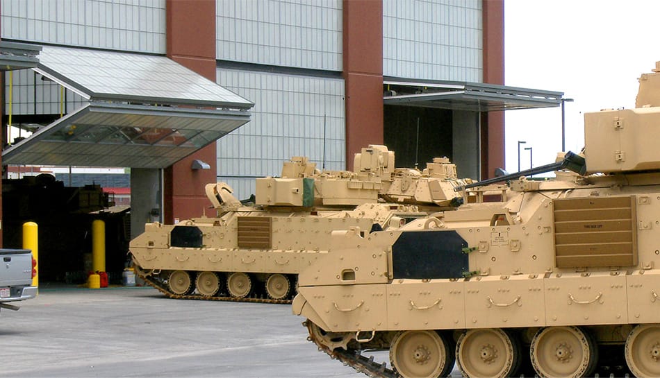 Multiple tank vehicles entering building fitted with multiple Schweiss bifold doors at Fort Carson