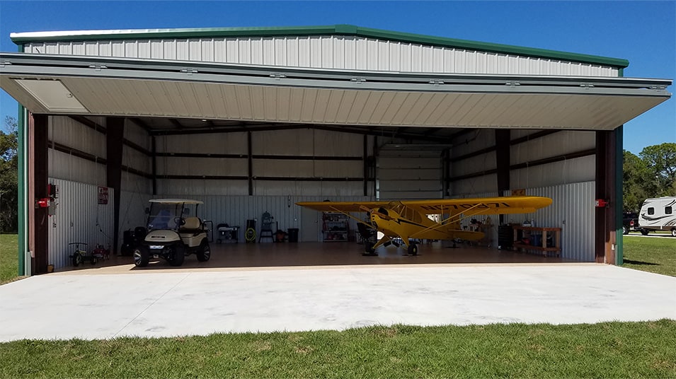 Schweiss bifold liftstrap door installed on Ray Cook's hangar shown open, a plane and golf cart parked inside