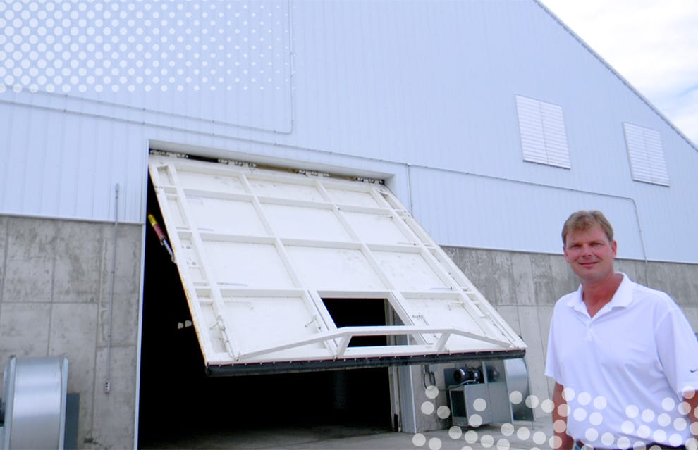 Tom Revier posed in front of Schweiss hydraulic door fitted on feed storage building at Revier Cattle Company