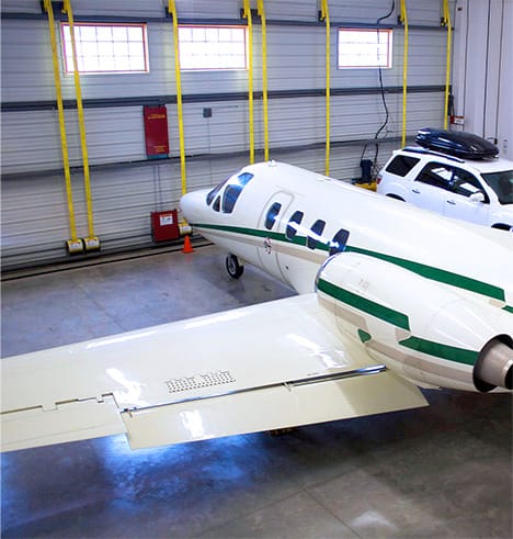 An airplane and minivan parked inside hangar fitted with a Schweiss bifold door at Silverwing Airpark