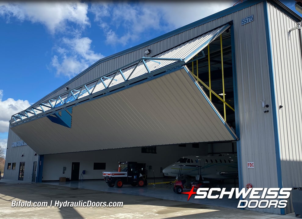 Exterior view of Schweiss bifold liftstrap hangar door fitted on SEI Hangar shown opening