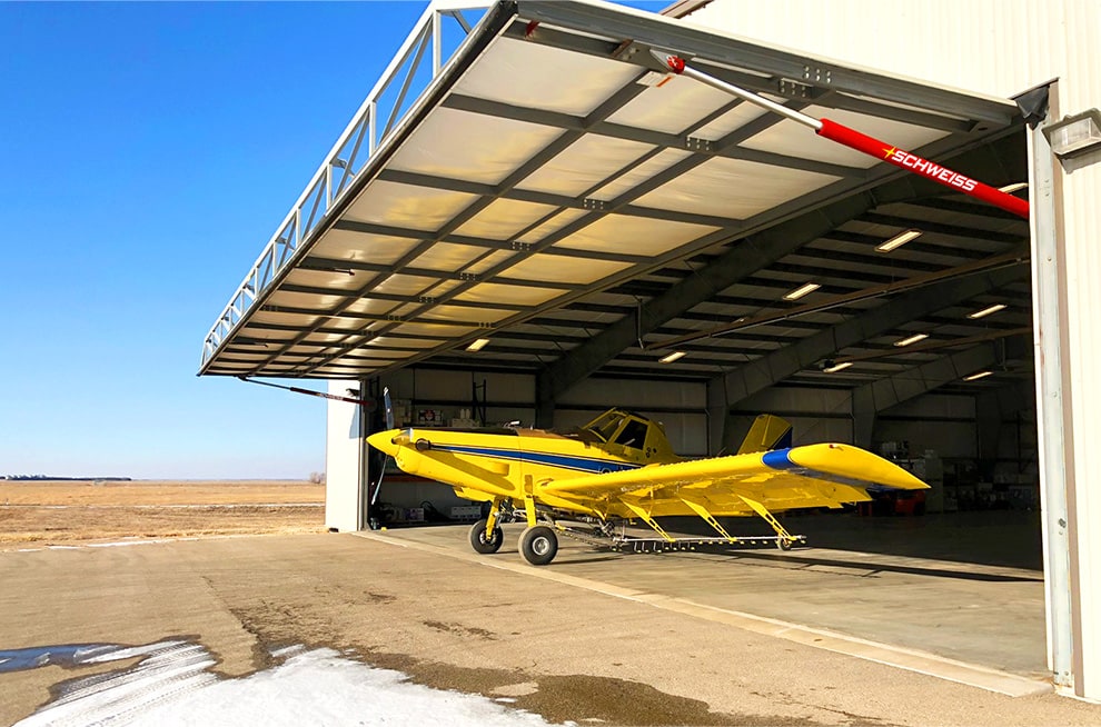 Yellow cropduster plane parked underneath opened Schweiss hydraulic door