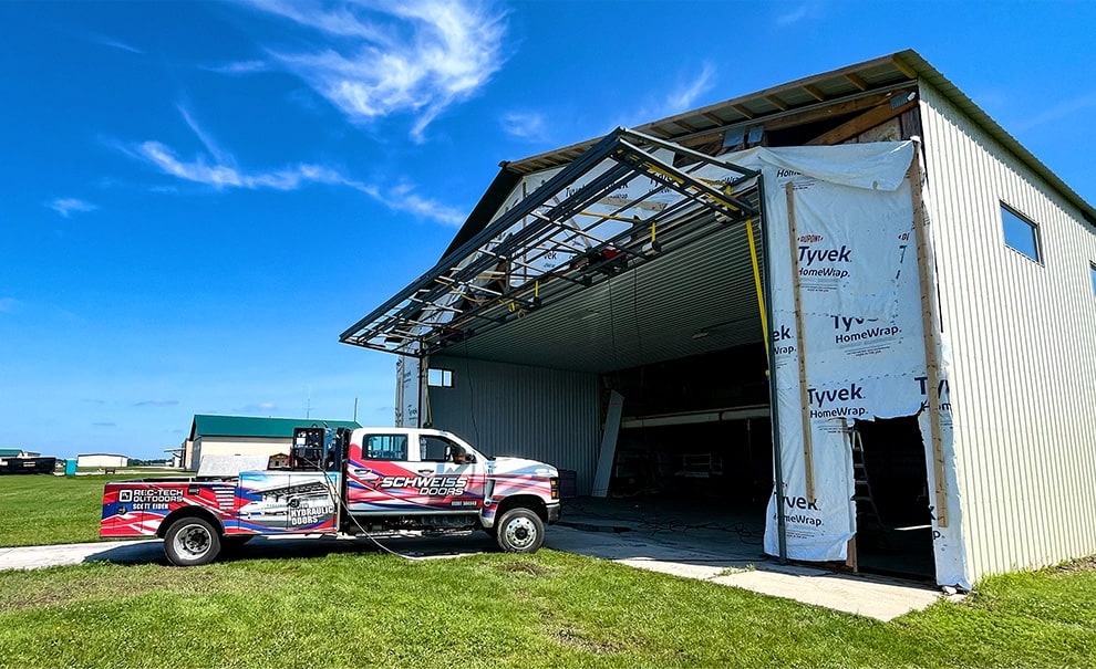 Schweiss installation truck parked outside newly built hangar that was just fitted a new Schweiss bifold lift strap door frame shown open