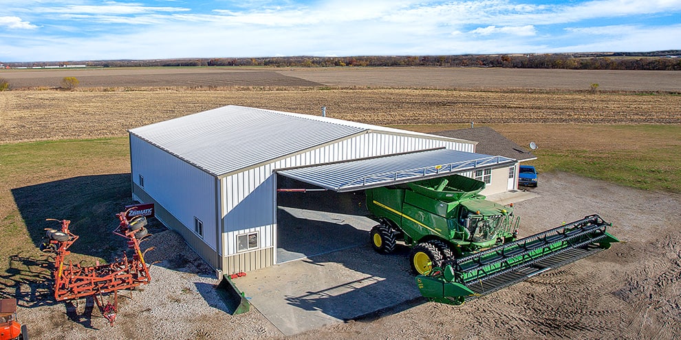 Farm combine parked underneath open Schweiss hydraulic door fitted on farm building