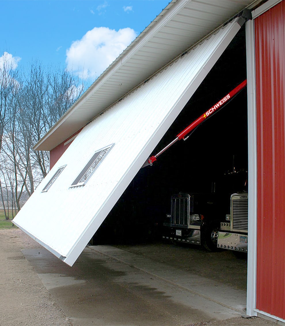 Exterior view of a Schweiss hydraulic door opening to reveal two semi trucks parked inside