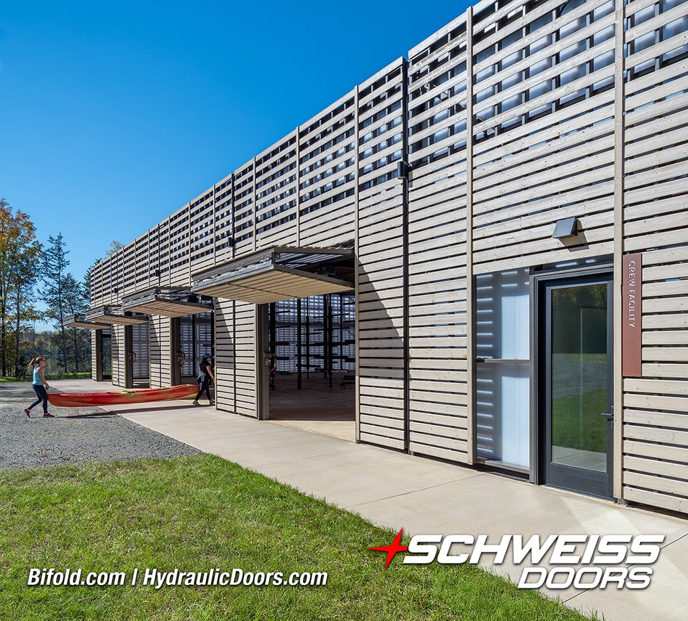Exterior view of 4 of 8 Schweiss bifold doors installed on Beaverdam Reservoir shown open, people carrying a rowing shell in through one