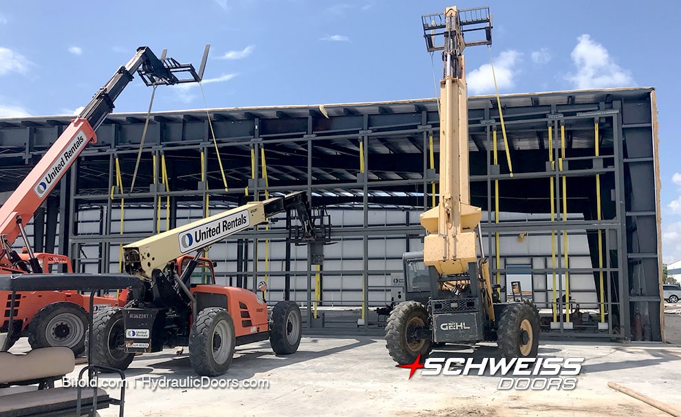 Three telehandlers being used to lift the Schweiss bifold doors into place on the new hangars at Pompano Beach Airpark