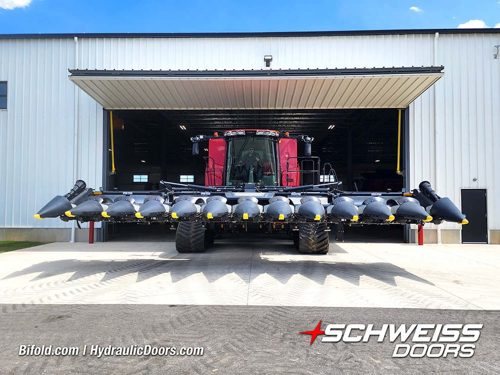 View from outside of a large combine driving out through Schweiss bifold liftstrap door on Redline Equipment building View from outside of a large combine driving out through Schweiss bifold liftstrap door on Redline Equipment building