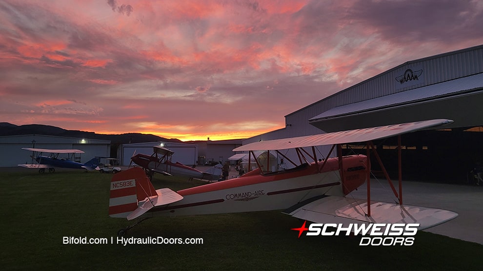 Command-Aire biplane and other aircraft parked outside hangars fitted with Schweiss bifold doors at sunset