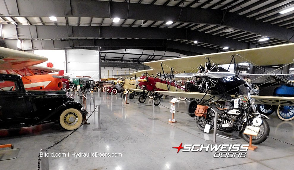 An assortment of automobiles, motorcycles, and planes from WAAAM's collection, stored in their hangar fitted with a Schweiss bifold door
