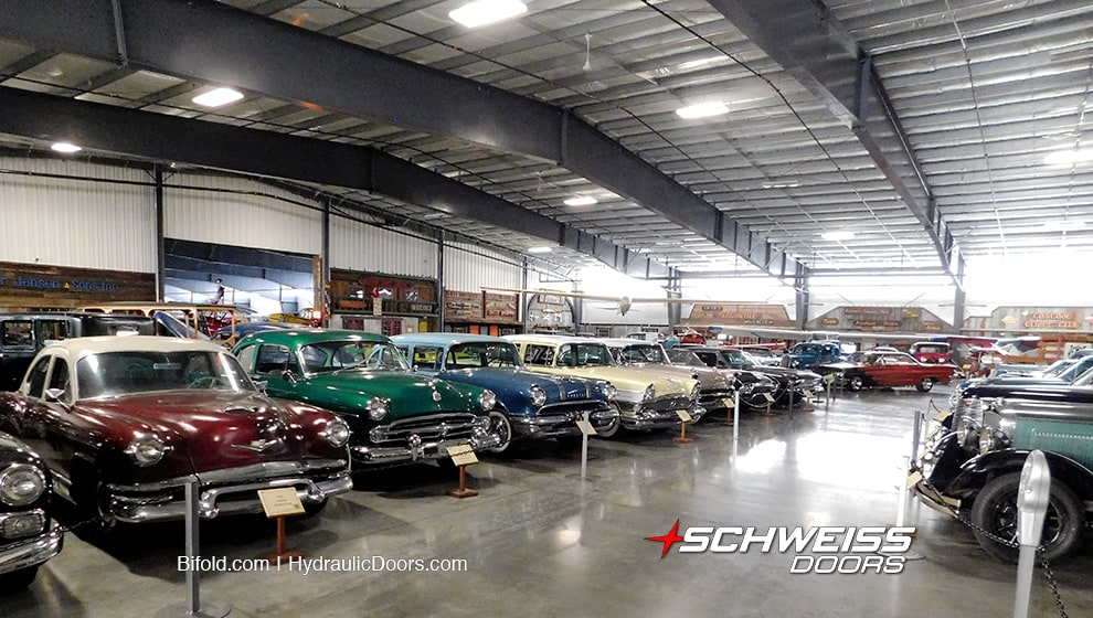 A variety of automobiles from WAAAM's collection, stored in their hangar fitted with a Schweiss bifold door